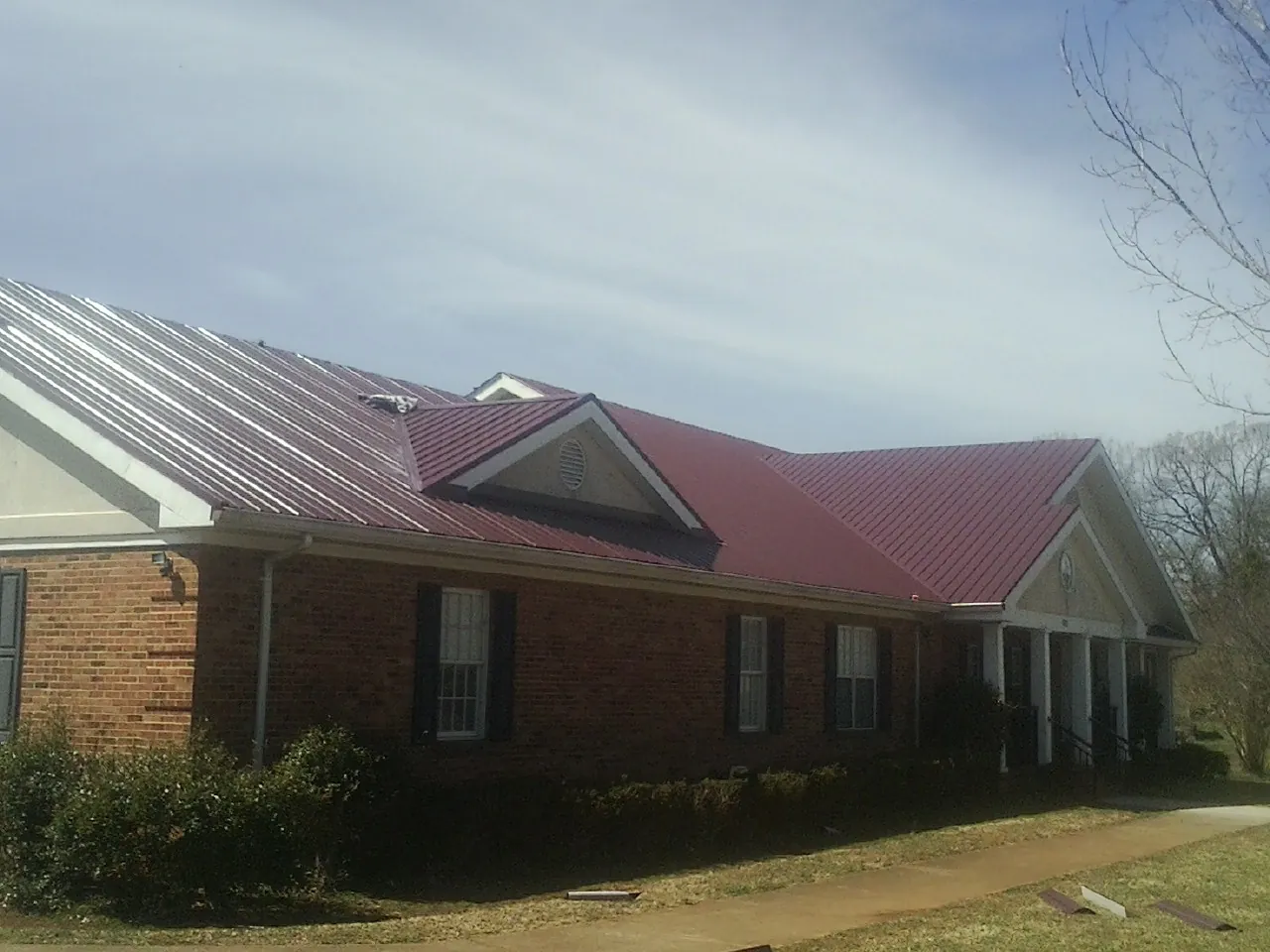 Red metal roof with gabled entries on a long brick building, from a Hail Damage Roof Repair job in Hazelton