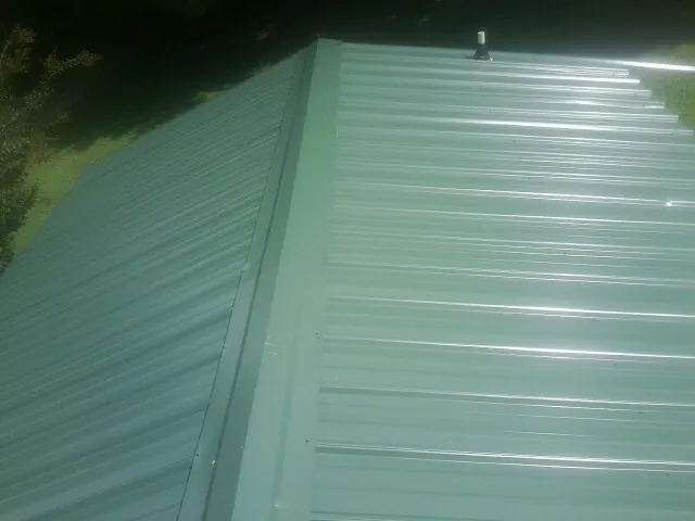 New green metal panels meeting at the ridge of a roof — Flat Roof Repair work by our crew in Hazelton
