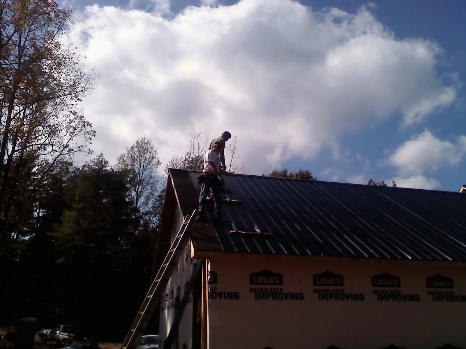 Roofer fastening dark metal panels high against a cloudy sky, from a Roof Inspection job in Hazelton